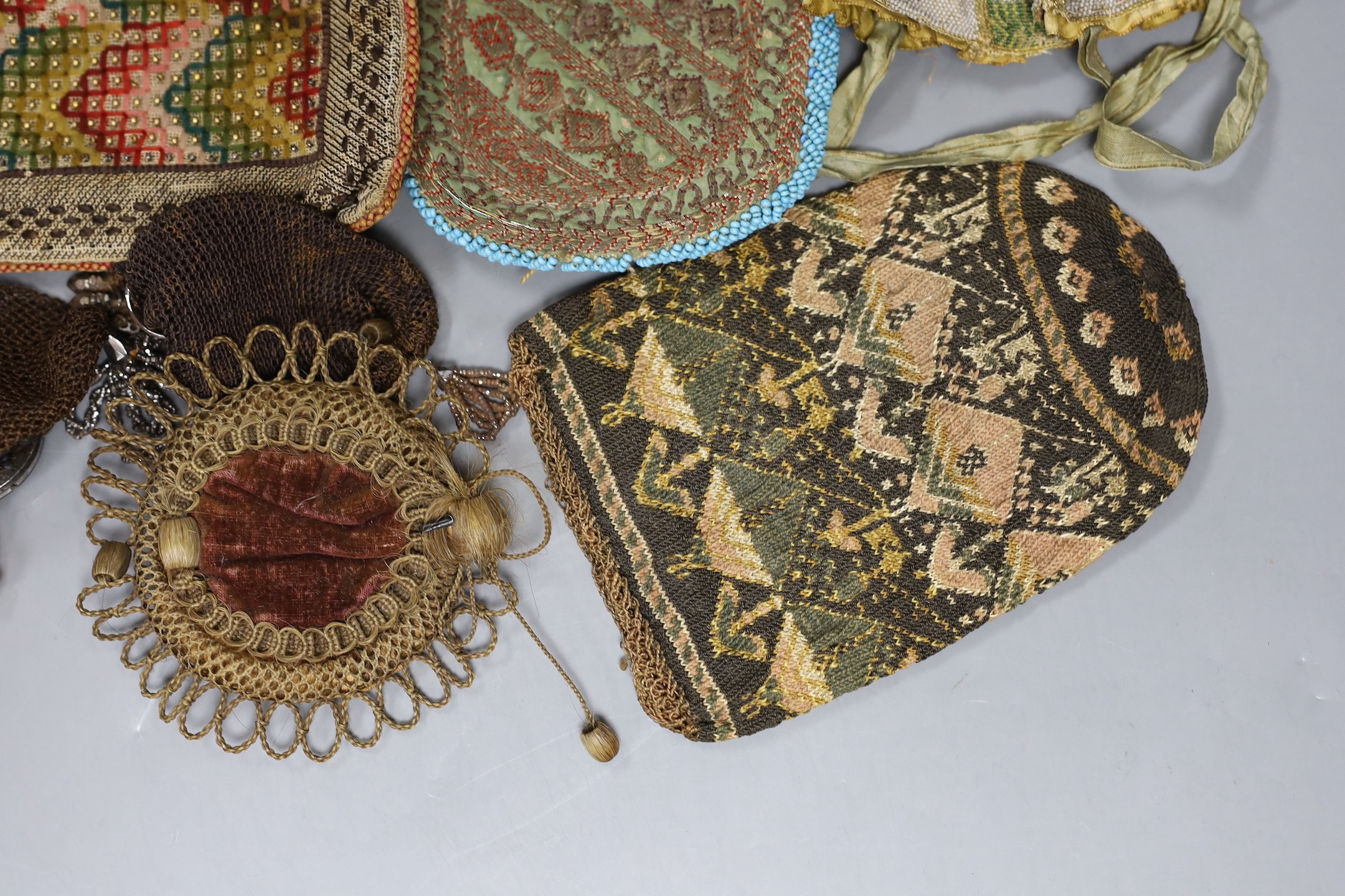 An early 19th century , possibly earlier, four sectioned floral bead worked reticule with ribbon handles, a hair and velvet pin cushion, a North African metallic embroidered bag, a similar bead and leather container, a k